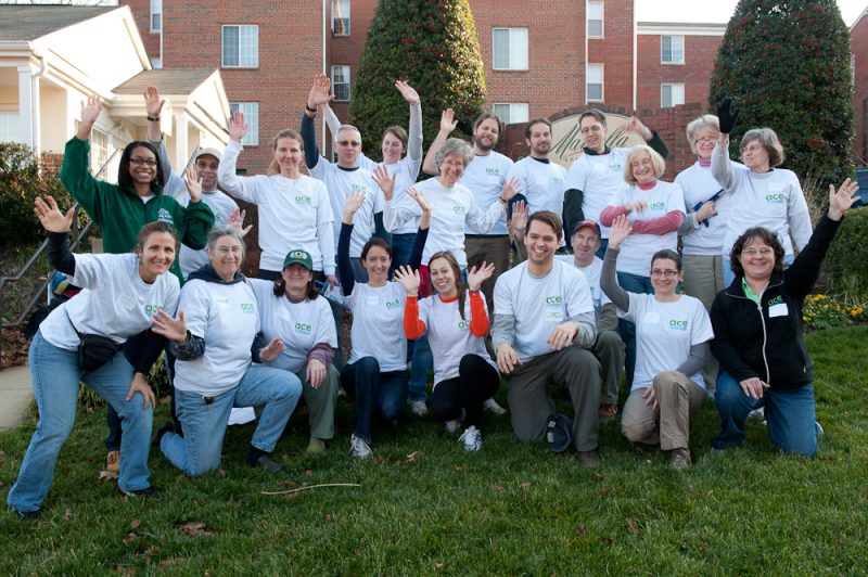 photo of a group of Energy Masters in branded t-shirts posed on grass in front of an apartment building and raising their hands in the air