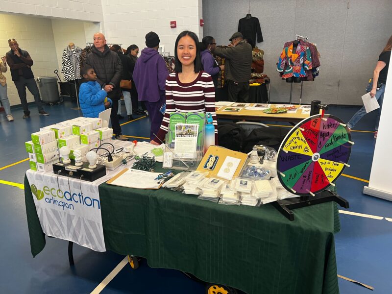 photo: Volunteer stands behind a branded table with information and a spin-the-wheel