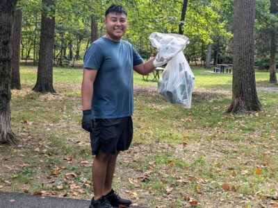 a volunteer holds up a garbage bag full of trash he collected at Barcroft park