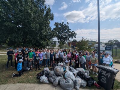 volunteers pose in front of bags of trash and debris collected at Barcroft park