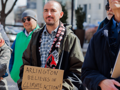 2025-Climate Resolution-1 six attendees of the rally on 2/22/205 gathered to hear speakers. A man in the front and center in blue and with plaid shirt, scarf and black bomber jacket holds a sign that reads: Arlington believes in climate action!