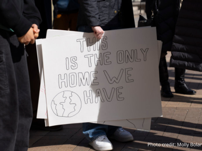 2025-Climate Resolution-15 Photo close up of sign at the rally on 2/22/2025 with attendees legs seen around the sign. Sign reads: Tis sis the only Home we have in large black block letters.