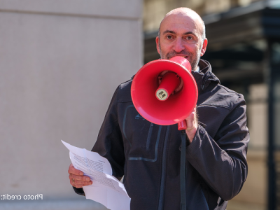 2025-Climate Resolution-9 close up of Mike Lowe, EcoAction Arlington Board Chair, speaking into a red megaphone. Photo credit: Bryan Scafford.