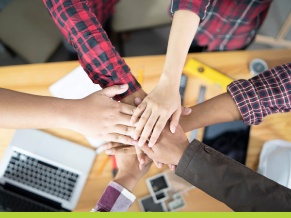 image of diverse arms with hands-in formation over a desk with laptops and notebooks