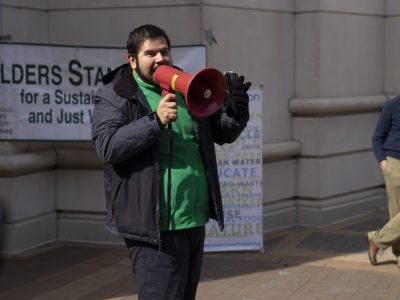 2025-climate resolution-50 Representative from Defensores de la cuenca holding a red megaphone and addressing the crowd at the climate resolution celebration rally.