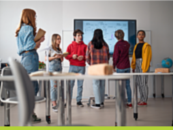 stock image of students gathered around a smartboard with a long desk in the foreground