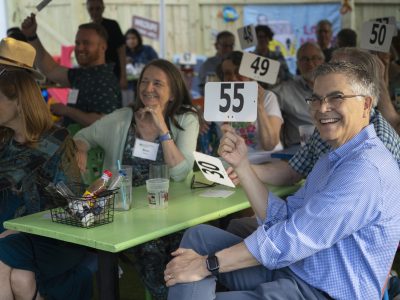 EcoExtravaganza guests sitting around tables holding up numbered paddles. Angelo Ioffredo is featured smiling in foreground