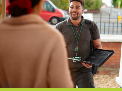 Gentleman in a polo shirt wearing a badge and holding device talks t a woman at the front door