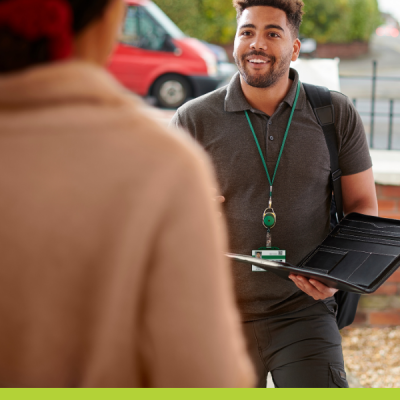 Gentleman in a polo shirt wearing a badge and holding device talks t a woman at the front door