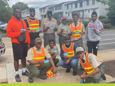 A group of volunteers in orange safety vests pose in front of storm drain marker that they have placed on a curb in Arlington