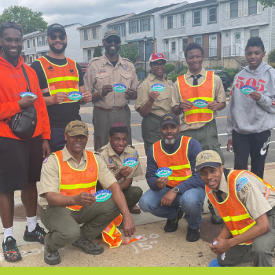 A group of volunteers in orange safety vests pose in front of storm drain marker that they have placed on a curb in Arlington