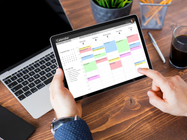 photo of hands selectin a date on a digital calendare with laptop, plant, pens and coffee on a desk