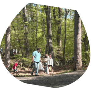 Man in blue shirt with 2 children picking up trash in a park setting with trees in the backgrouns