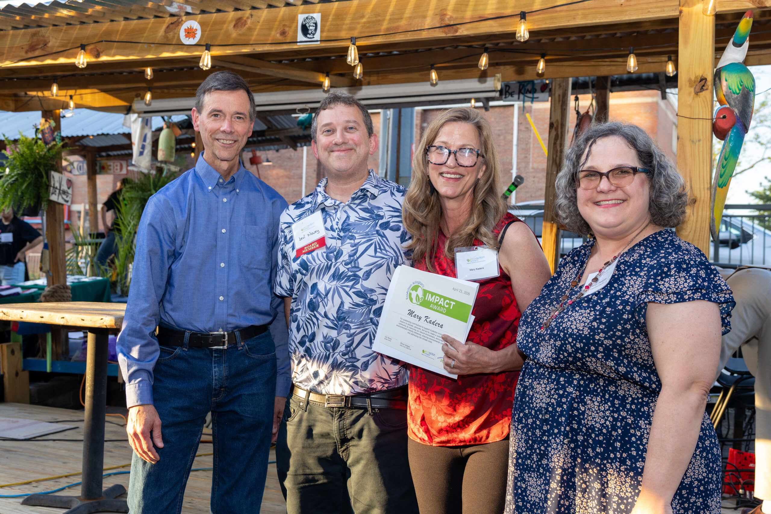 John Bloom, Levi Novey, Mary Kadera holding the certificate award and Elenor Hodges posing in front of tike-themed stage on Clare & Don's Beach Shack back patio