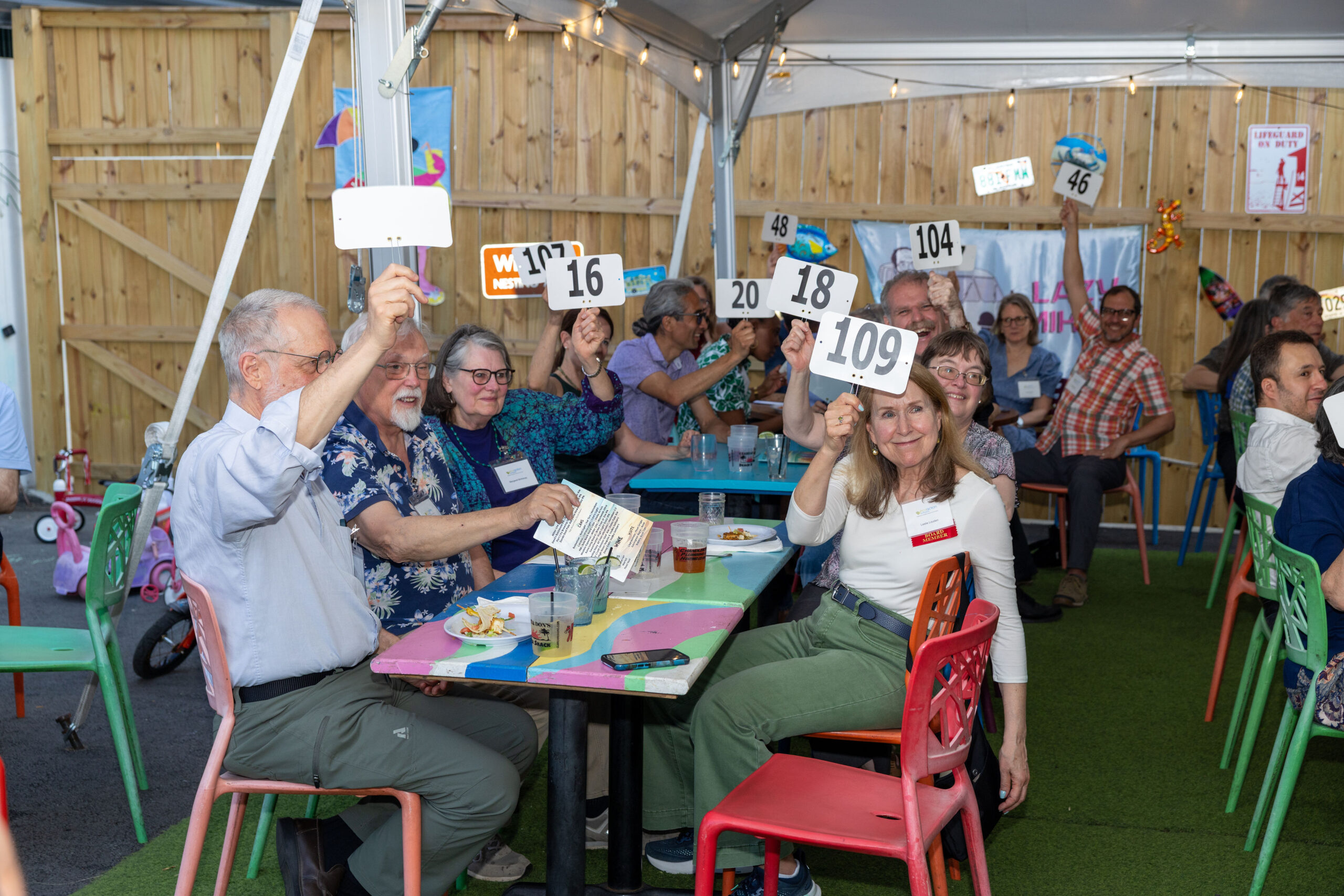 Group of men and women sitting on colorful chairs around a table raising paddles with numbers on them