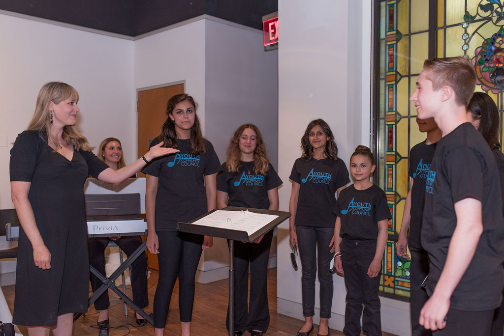 photo of youth choral group singing in front of music stands wearing coordinated t-shirts