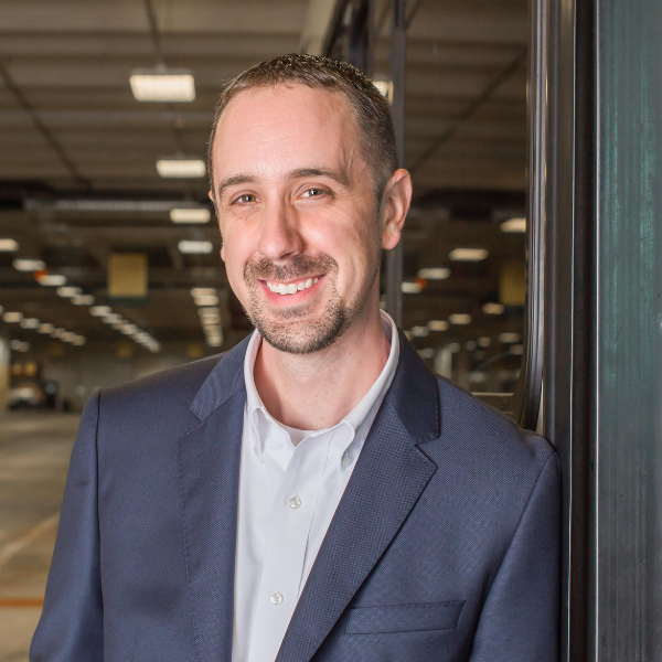 headshot of Joshua Bakers a man with a van dyke smiling at camera whering a cadet blue suit and grey dress shirt