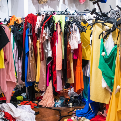 many colorful items of clothing overflowing in a walk-in closet with piles of clothes and shoes on the floor